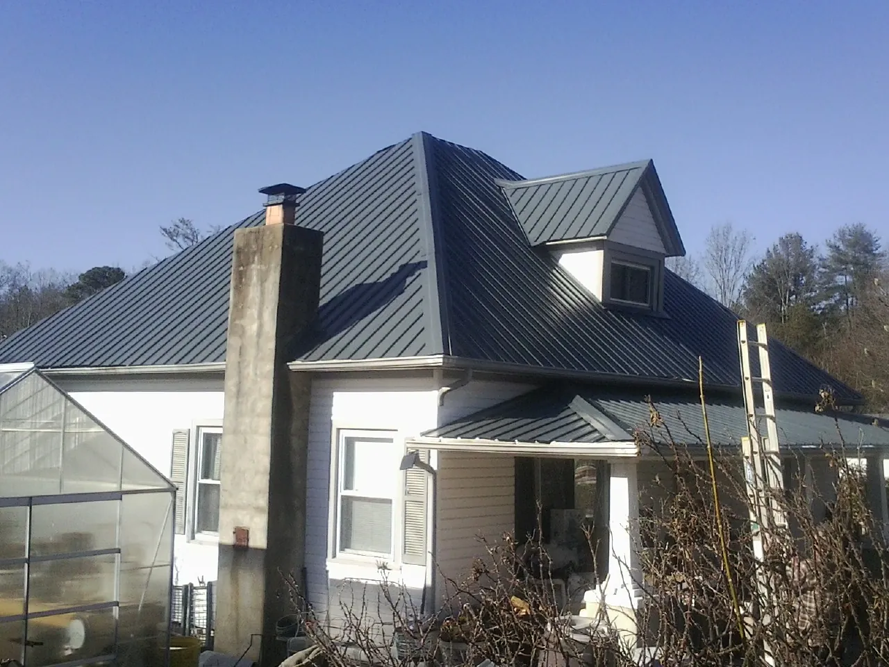 Dark blue standing seam metal roof on a white farmhouse with dormer — Slate & Tile Roof Repair by Roofing Brothers in Barney