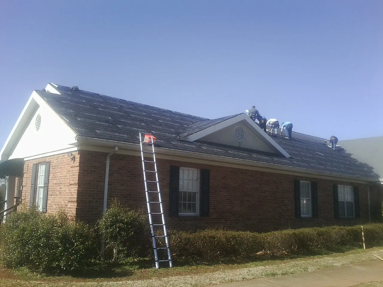 Crew tearing shingles off a brick ranch roof with a ladder set — Emergency Roof Repair work by our crew in Barney