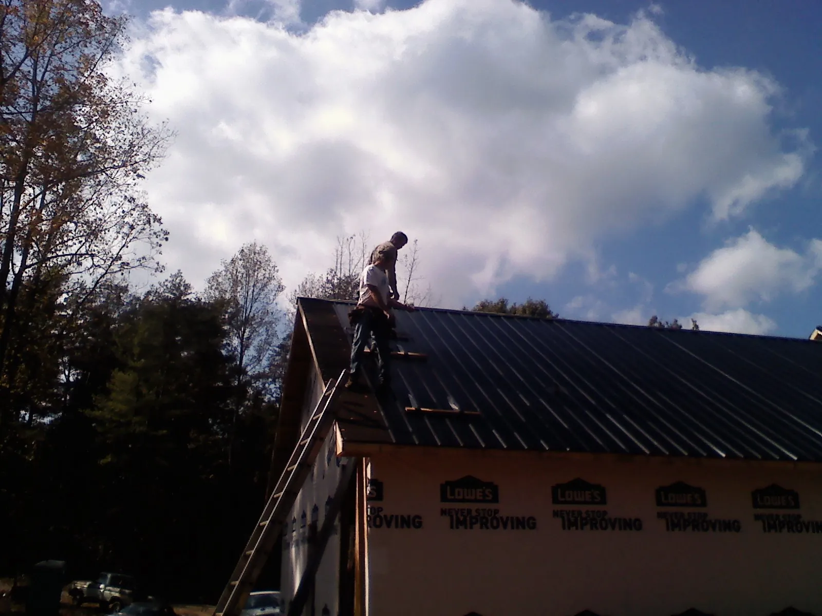 Roofer fastening dark metal panels high against a cloudy sky, from a Roof Inspection job in Barney